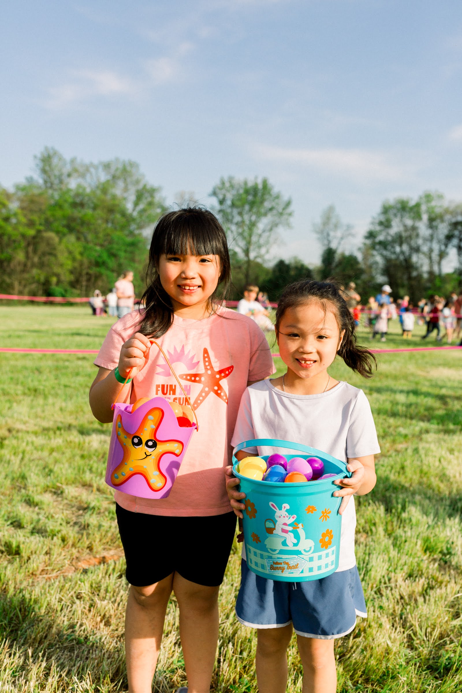 two children posing with Easter baskets full of Easter eggs. Children are standing on a field where they hunted the eggs